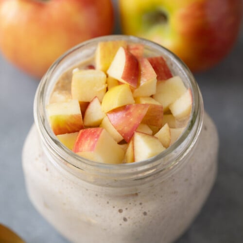 A jar of apple pie overnight oats with apples in the background
