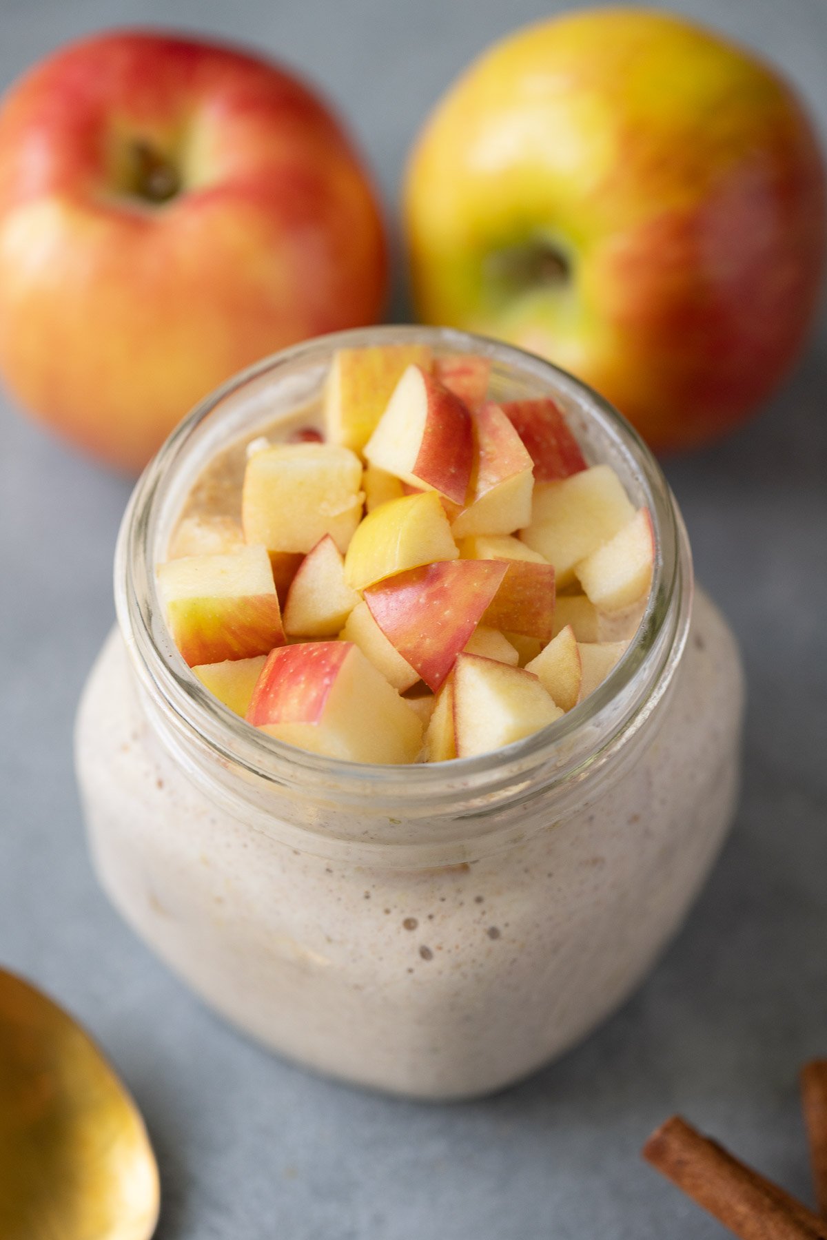 A jar of apple pie overnight oats with apples in the background