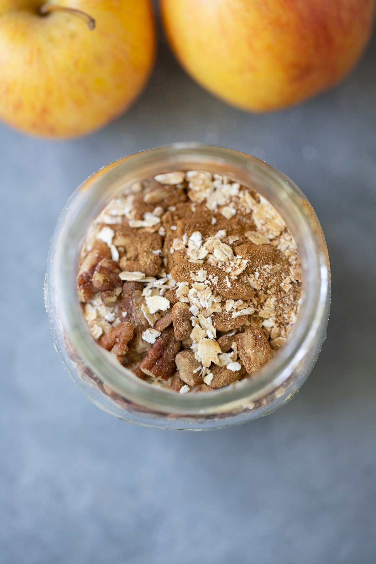An overhead shot of a mason jar filled with overnight oats before being stirred for apple overnight oats on a grey background