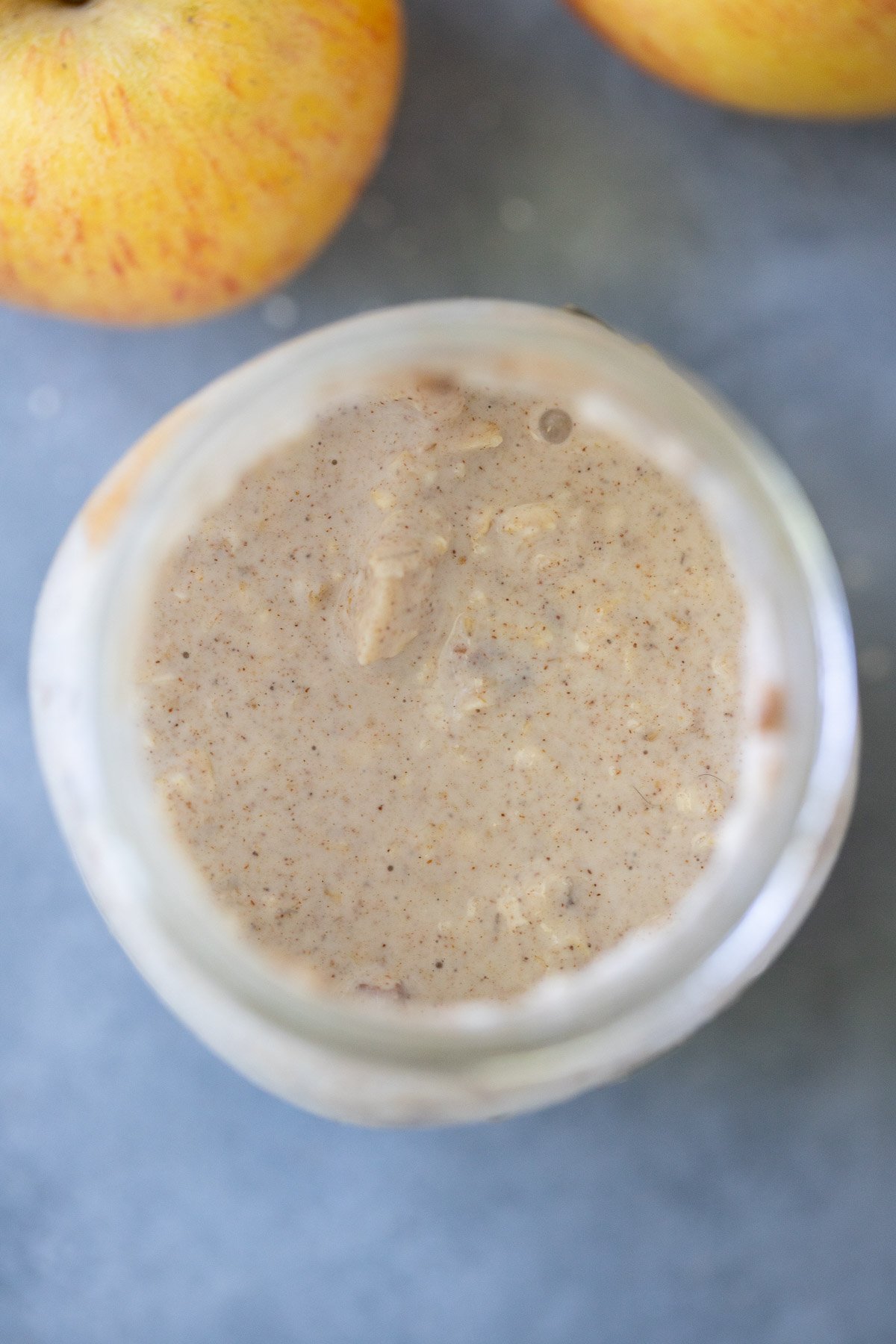 An overhead shot of a mason jar filled with overnight oats after stirring for apple overnight oats on a grey background