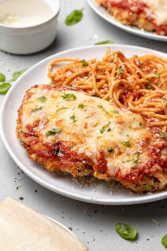 A side view of a plate of baked chicken parmesan with pasta