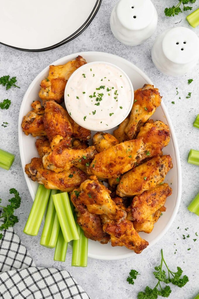 A platter of Baked Chicken Wings with celery on the side on a white background.