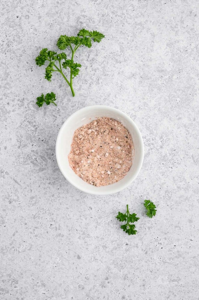 Spices (cornstarch, salt, pepper, paprika, garlic powder) for Crispy Baked Chicken Wings in a small white bowl on a grey background. 