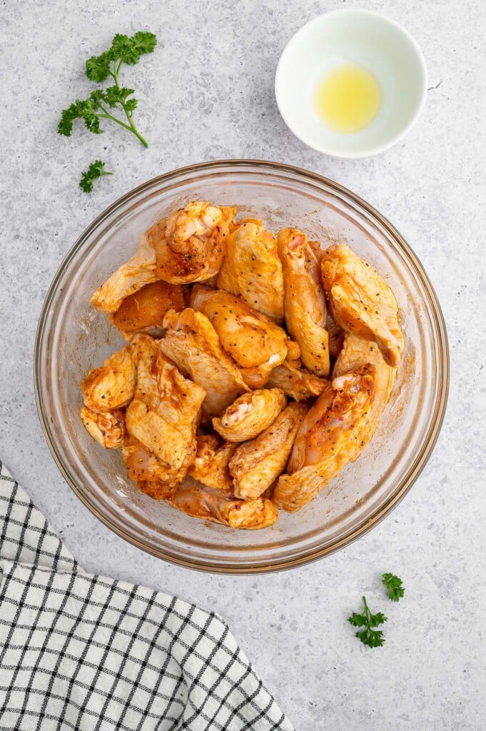 Seasoned Raw Chicken Wings in a clear bowl with another bowl on the side on a grey background.