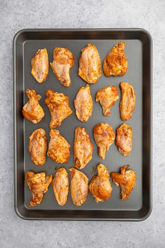 Raw Chicken Wings on a baking sheet before baking on a grey background. 