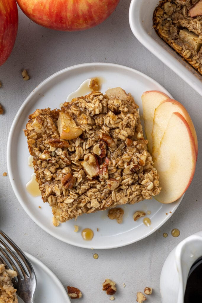 A close up of healthy baked oatmeal on a white plate with apples off to the side