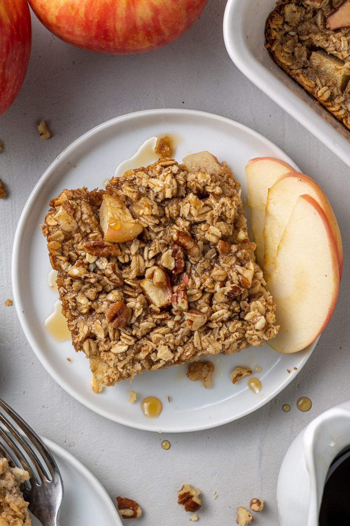 A close up of healthy baked oatmeal on a white plate with apples off to the side