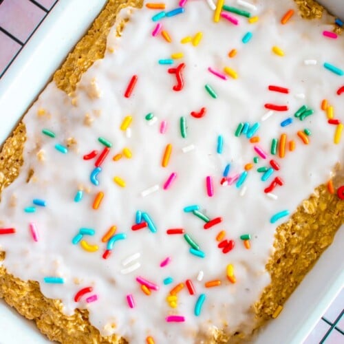An overhead shot of baked oats in a white baking dish topped with white frosting and sprinkles