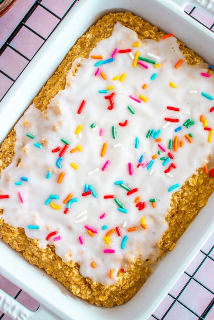 An overhead shot of baked oats in a white baking dish topped with white frosting and sprinkles