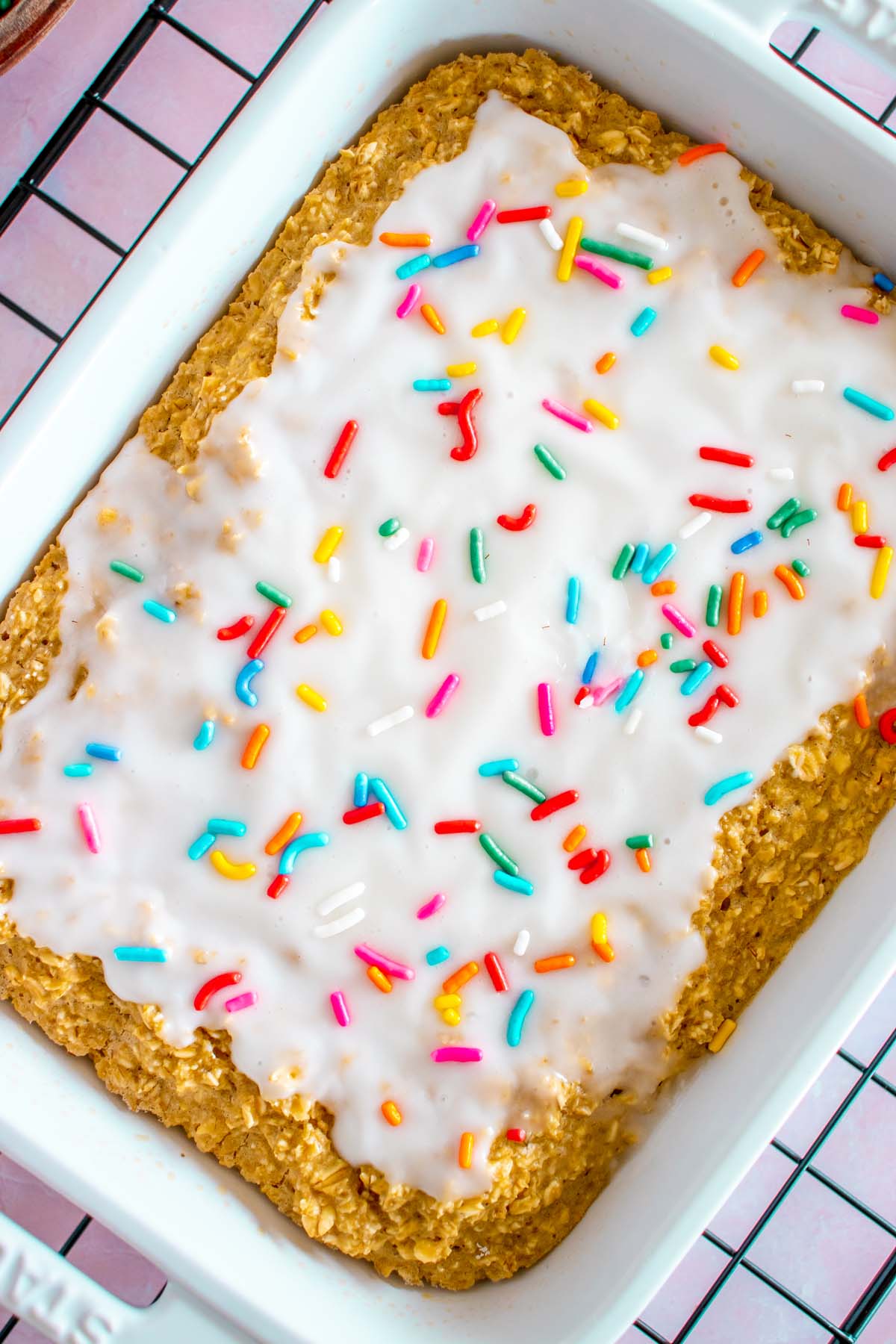 An overhead shot of baked oats in a white baking dish topped with white frosting and sprinkles