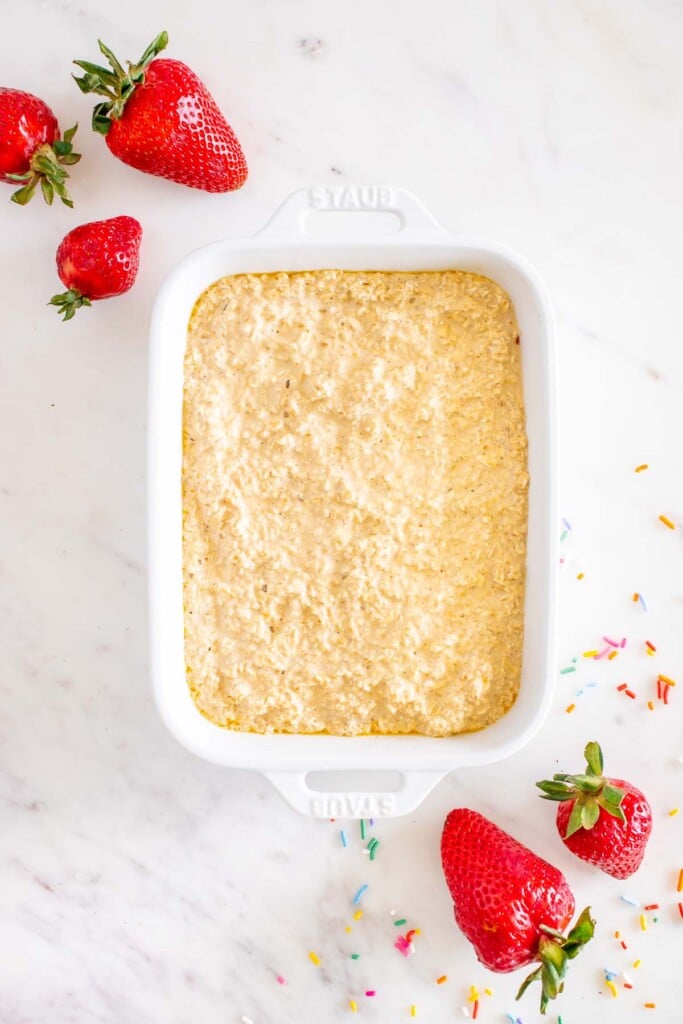 uncooked baked oats in a white baking dish with strawberries on the side