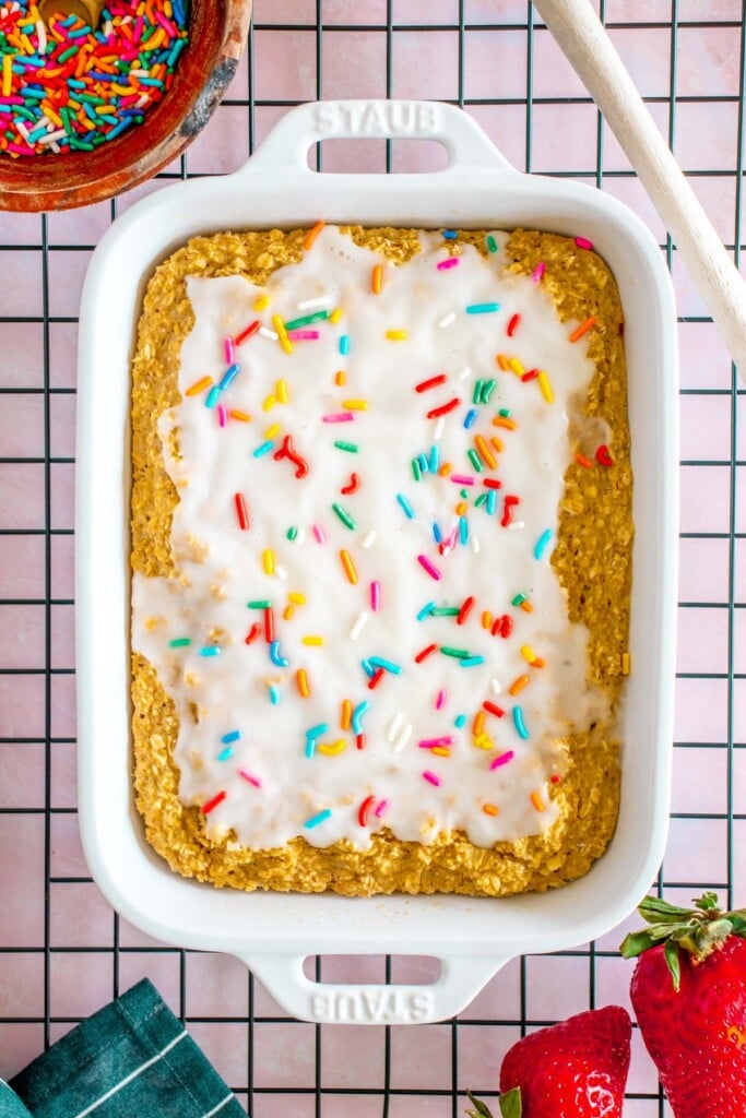 An overhead shot of baked oats in a white baking dish that has vanilla frosting on top with sprinkles on it 