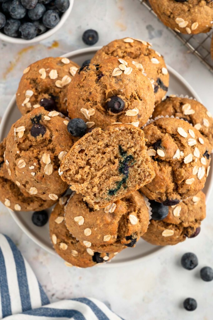 An overhead shot of a plate full of blueberry banana muffins with blueberries near it on a white background