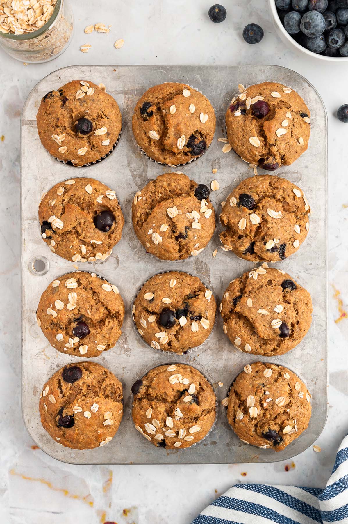 An overhead of a lined muffin pan with 12 blueberry banana muffin tin after baking on a marble background