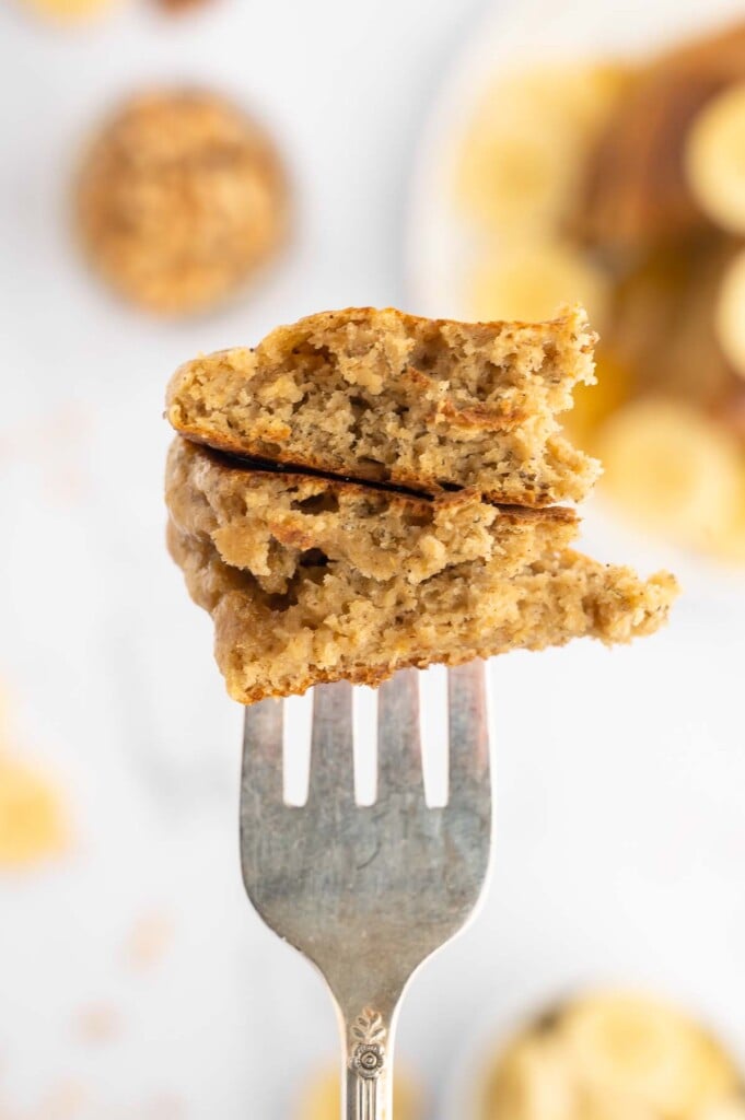 A bite of healthy banana pancakes on a fork with the plate of pancakes blurry in the background