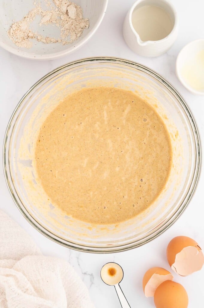 An overhead shot of banana pancake batter in a clear bowl on a marble counter