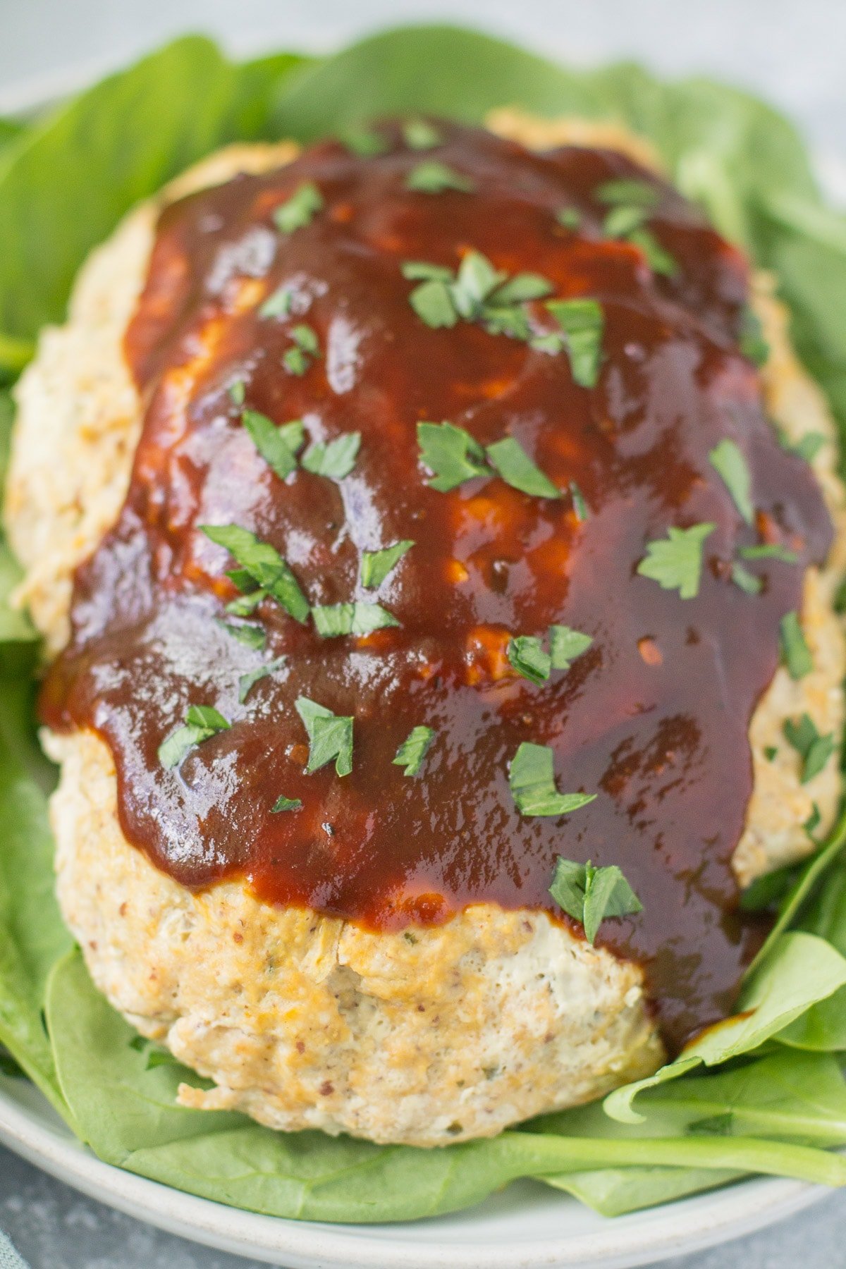A close up of BBQ Chicken Meatloaf on a white plate with spinach