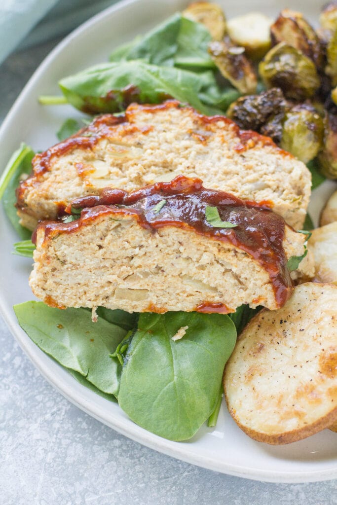 Sliced BBQ Chicken Meatloaf on a white plate with roasted potatoes and spinach