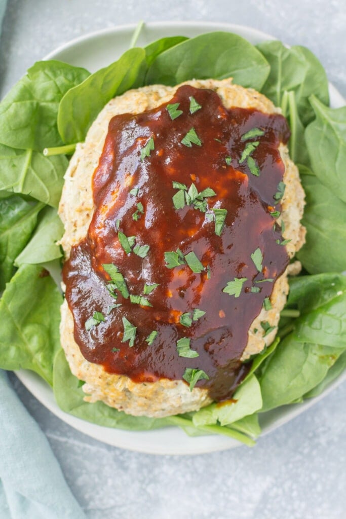 An overhead shot of instant pot meatloaf on a spinach lined white plate on a grey background.