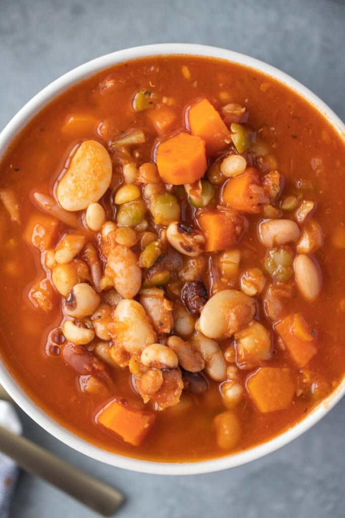 a close up of 15 bean soup in a white large bowl on a grey background