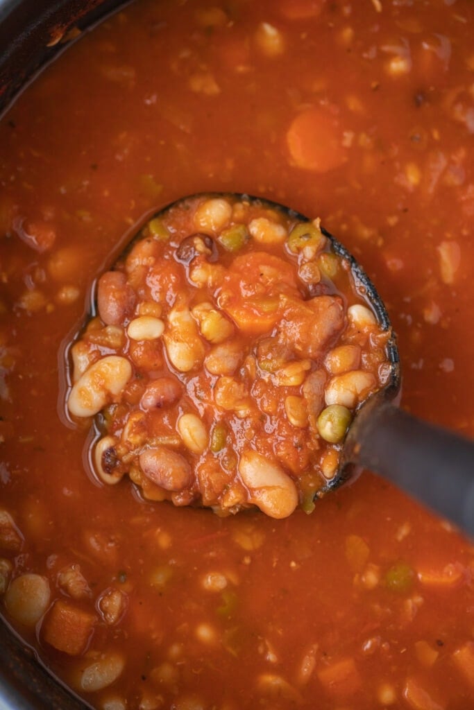 a ladle taking a scoop out of a dutch oven of 15 bean soup