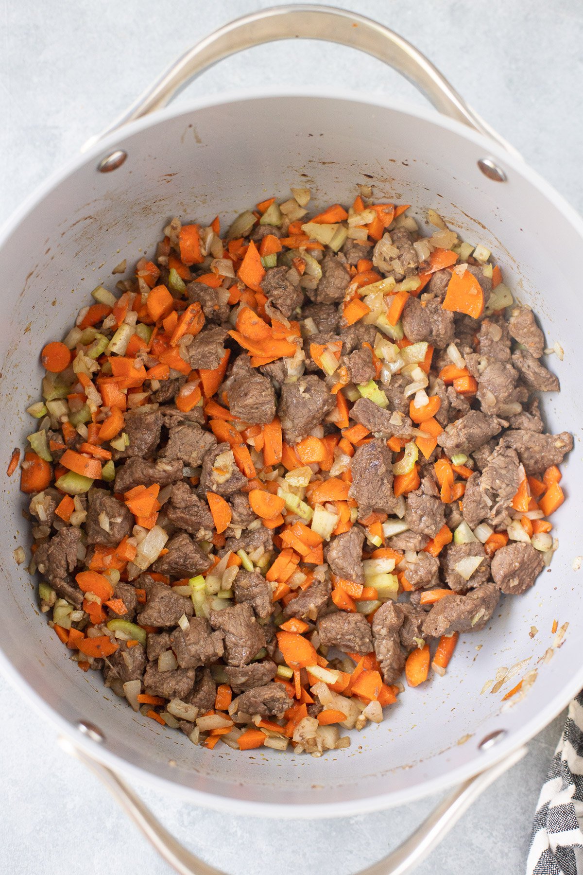 Beef and veggies in a pot for beef barley soup on a grey background