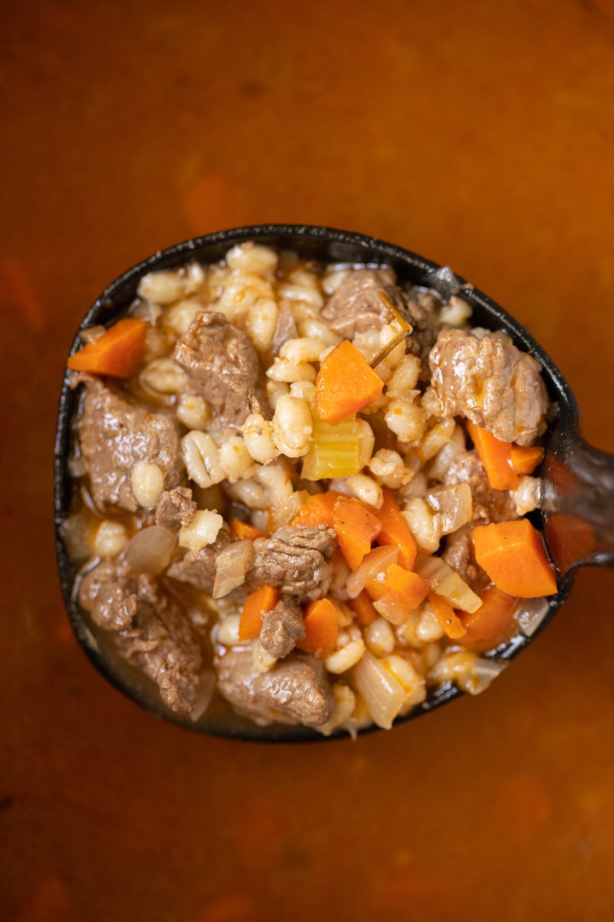 A ladle taking a large scoop of beef barley soup out of a pot