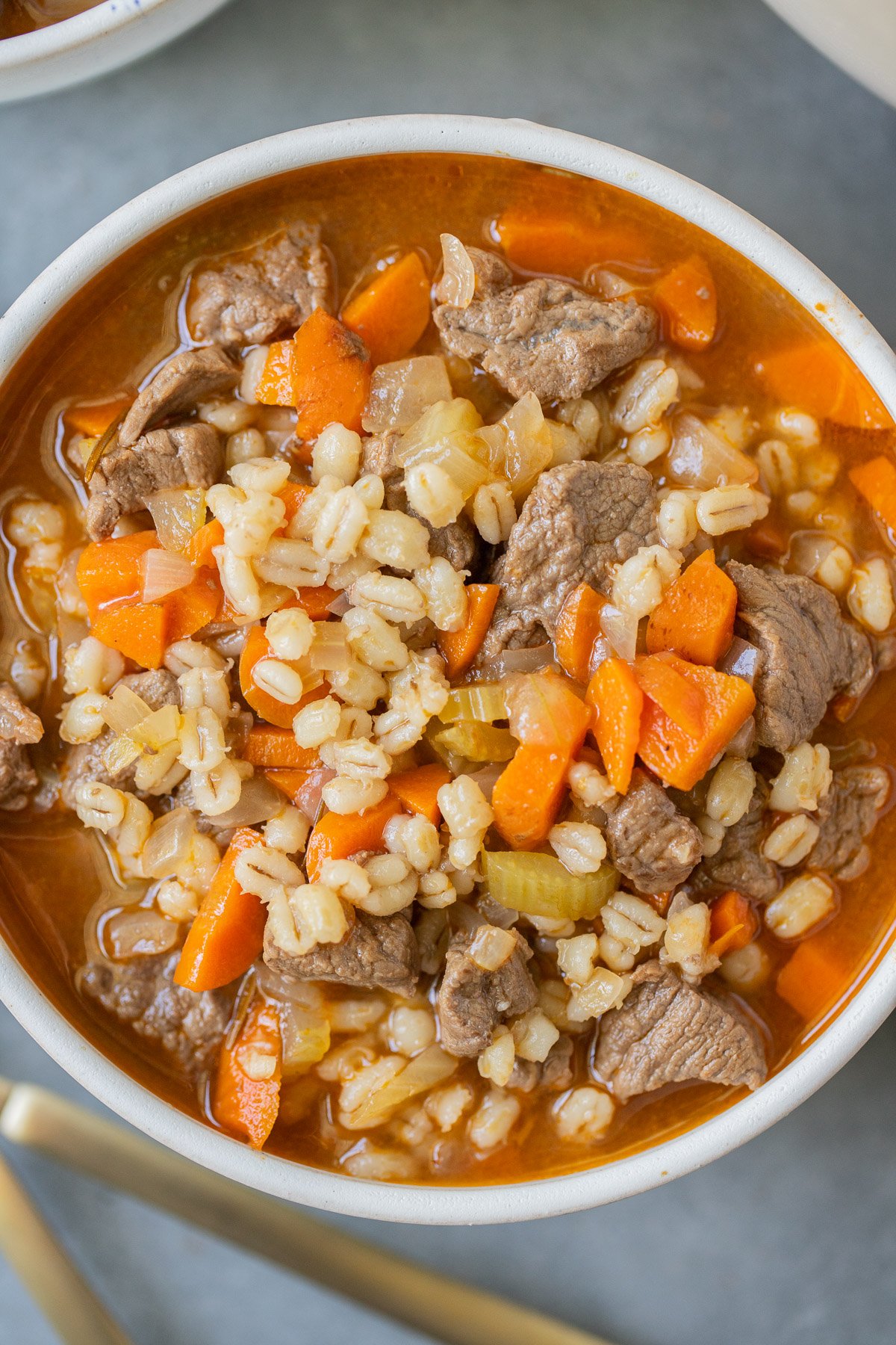 An overhead shot of a bowl of beef barley soup on a grey background