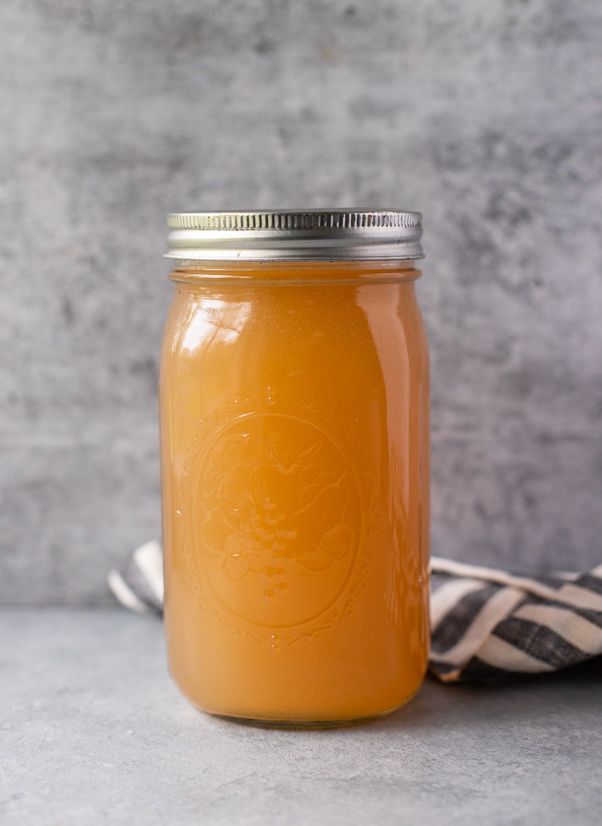 Bee Bone Broth in a glass jar on a grey background with a lined linen in the back