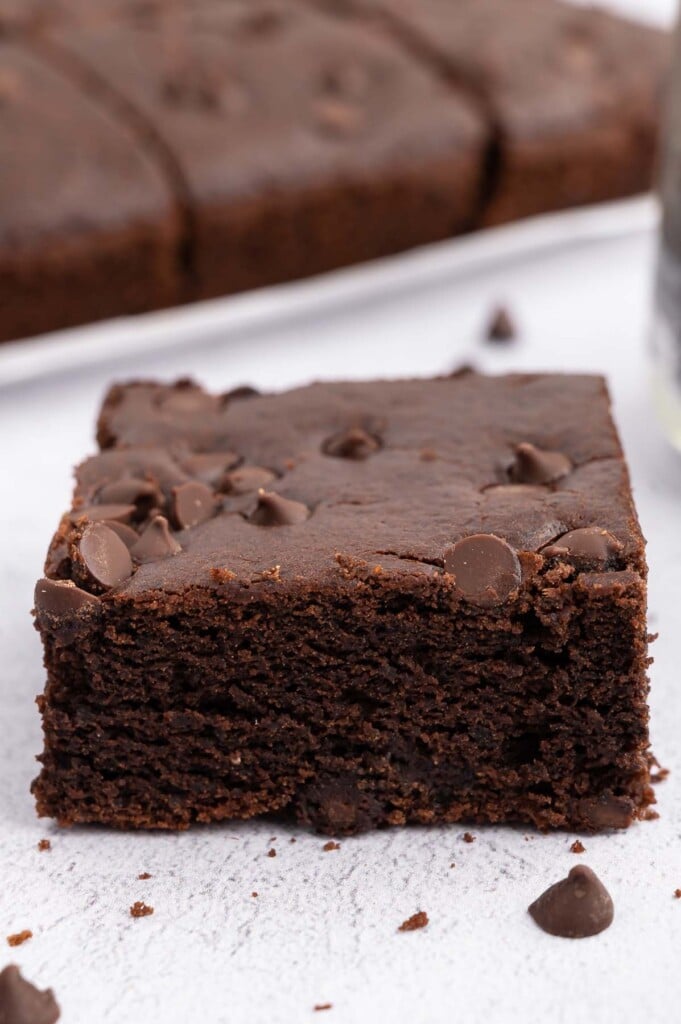 A black bean brownies with a pan of healthy brownies in the background on a white counter
