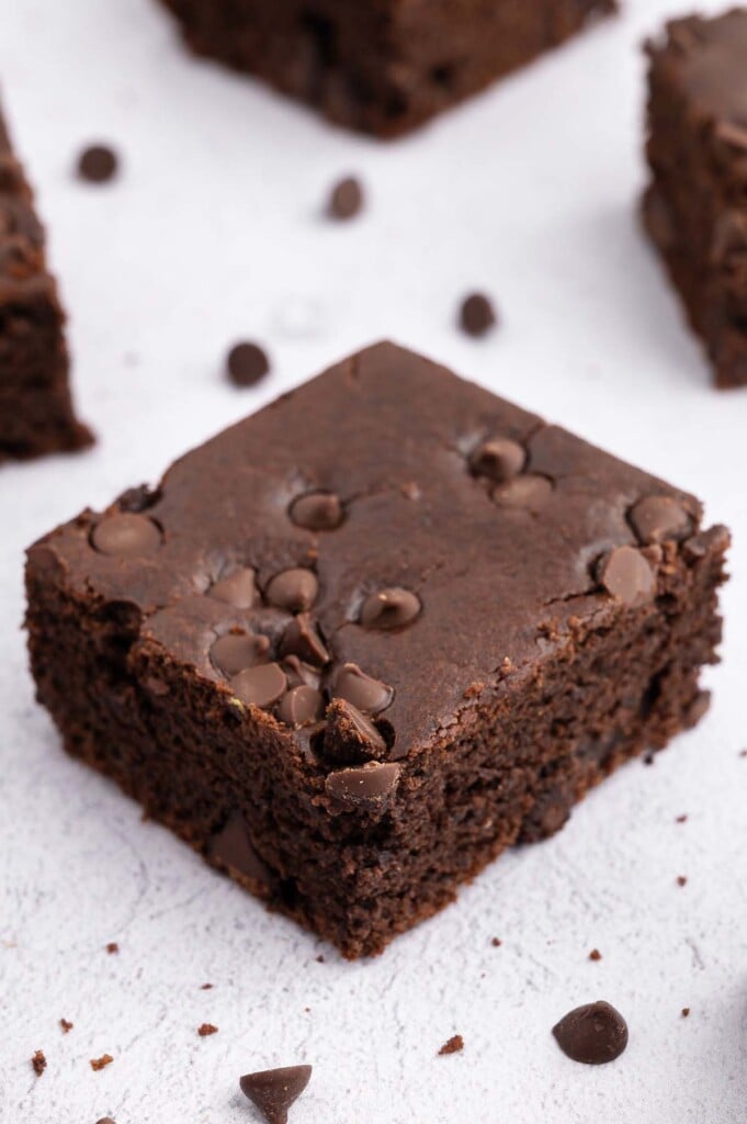 One black bean brownie on a white background with mini chocolate chips and more brownies in the background