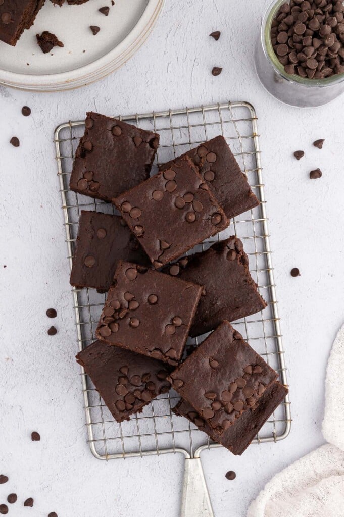 An overhead shot of black bean brownies on a cooling rack on a white background surrounded by mini chocolate chips