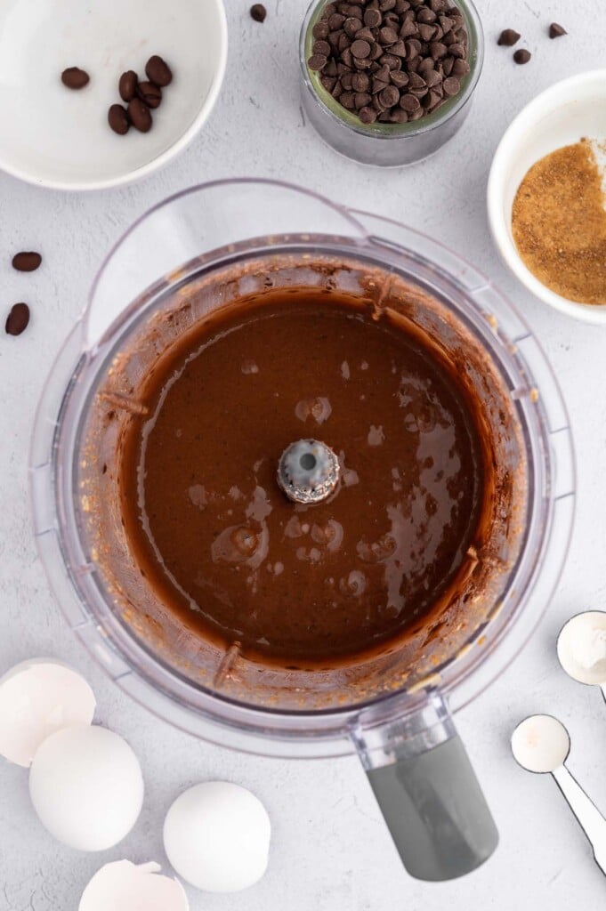 A food processor filled with blended black bean brownie batter with chocolate chips on the side