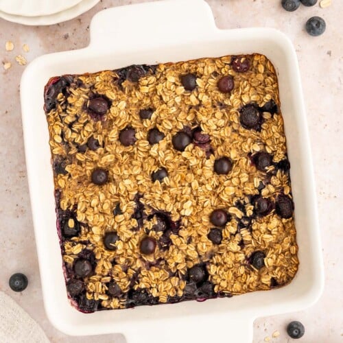 A white baking dish of Healthy Blueberry Baked Oatmeal with blueberries on the side.