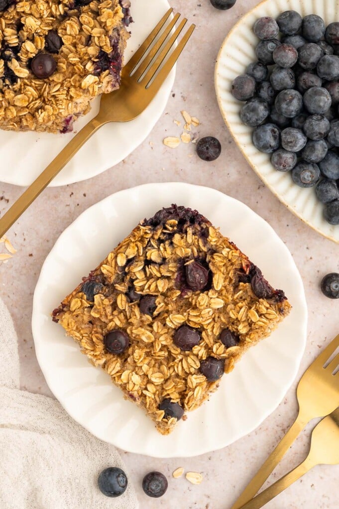 An overhead shot of blueberry baked oatmeal on a white plate with another plate and blueberries on the side.