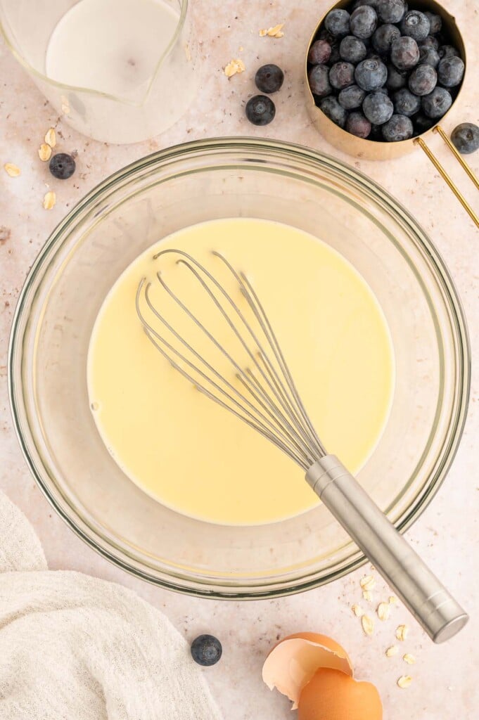 Wet ingredients for blueberry baked oatmeal in a clear bowl with a whisk.