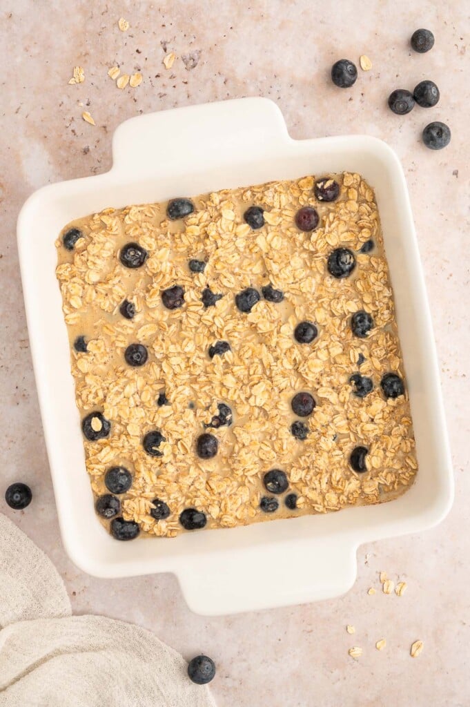 Uncooked blueberry baked oatmeal in a white square baking dish. 