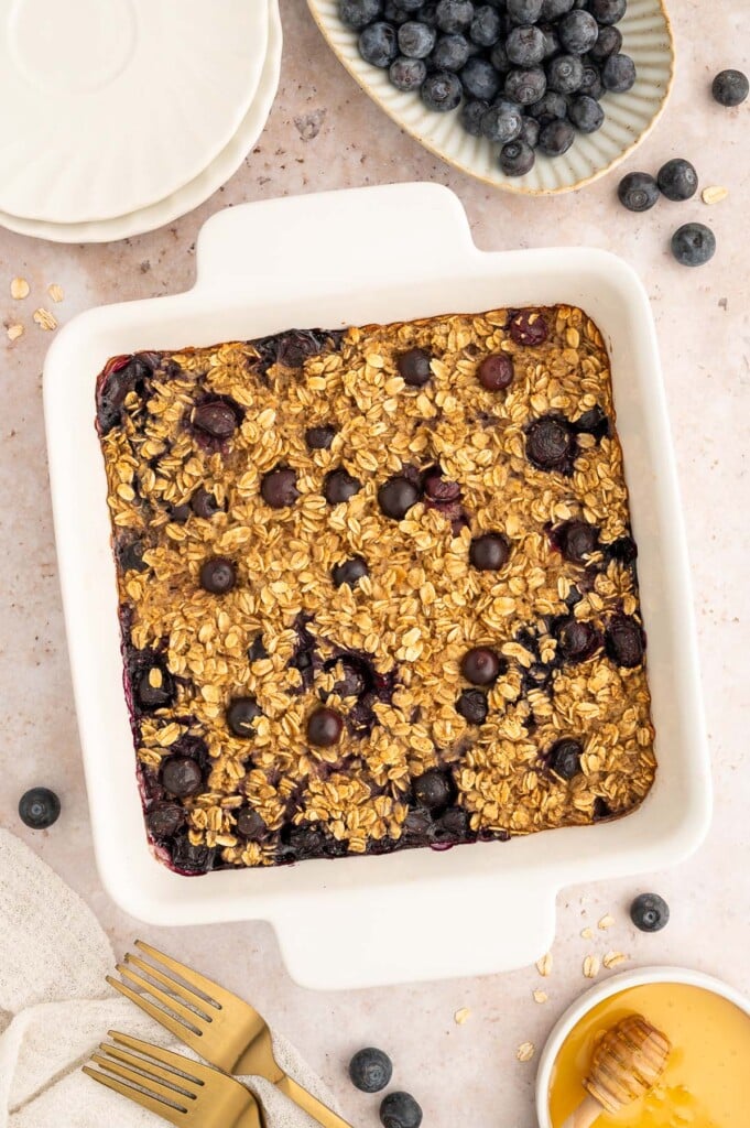A white baking dish of Healthy Blueberry Baked Oatmeal with blueberries on the side.