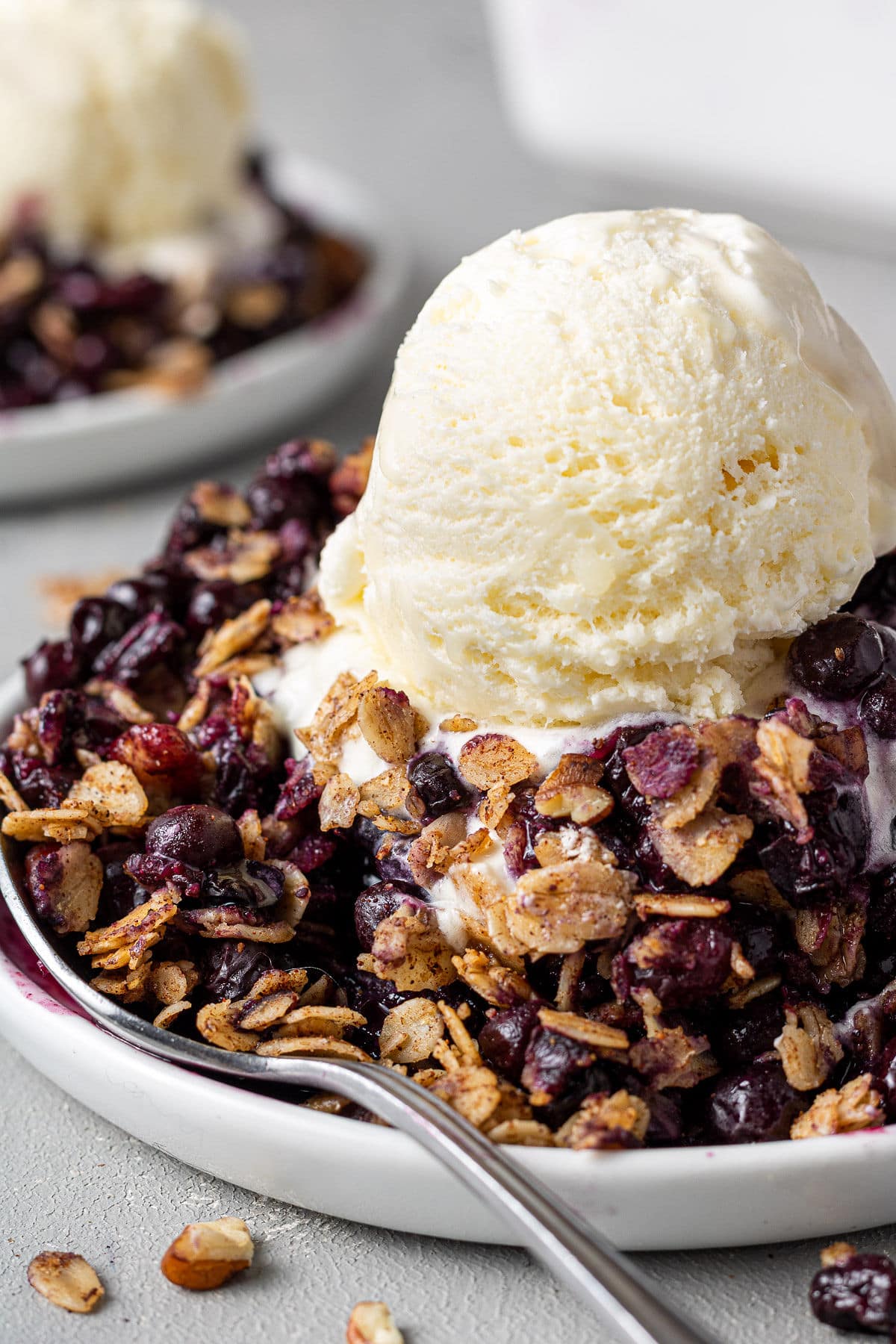 Healthy Blueberry Crisp on a white dish with a scoop of vanilla ice cream