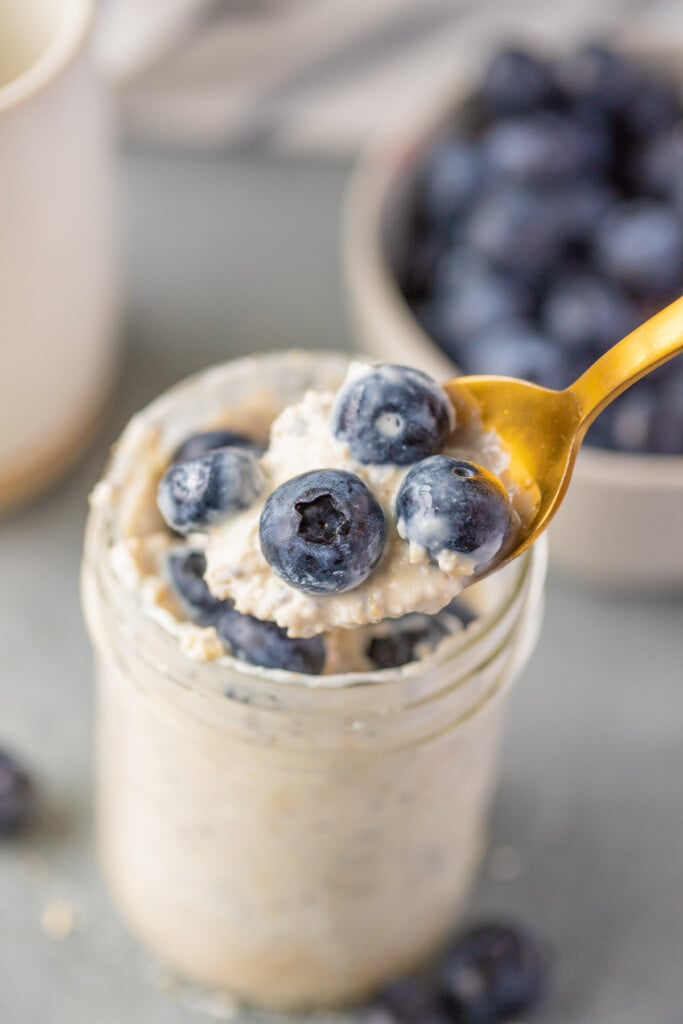 A gold spoon taking a bite out of a mason jar of blueberry overnight oats