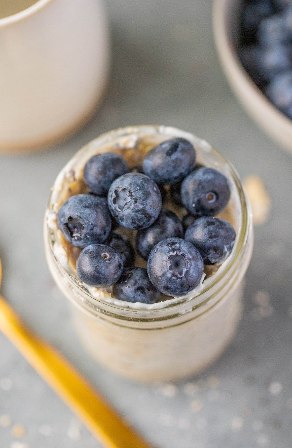 An overhead image of overnight blueberry oats on top of a grey background with a gold spoon on the side