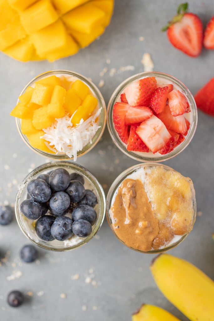An overhead shot of four mason jars of overnight oats: mango overnight oats, strawberry overnight oats, blueberry overnight oats, banana overnight oats