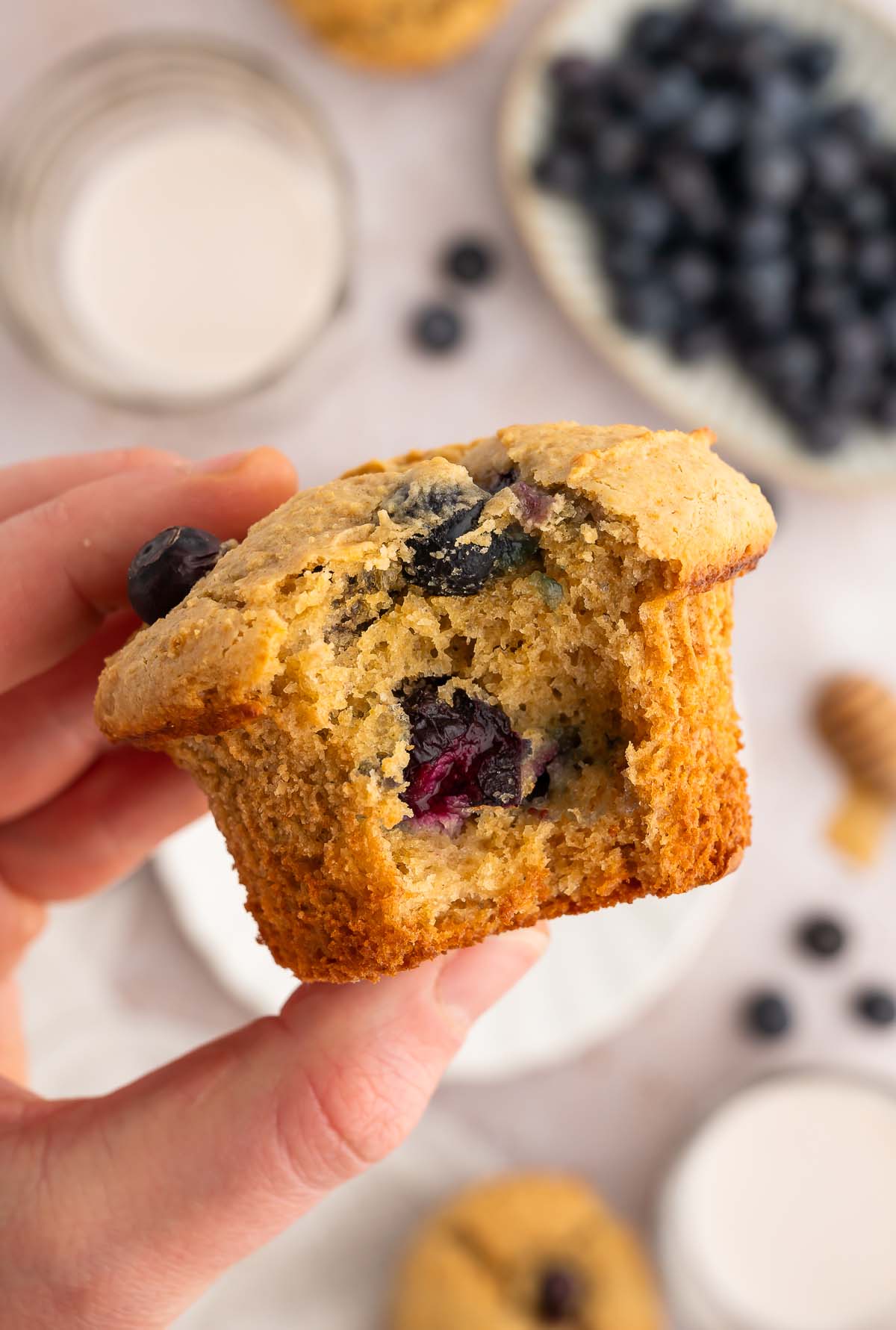 A hand holding up a blueberry protein muffin with a bite taken out of it.