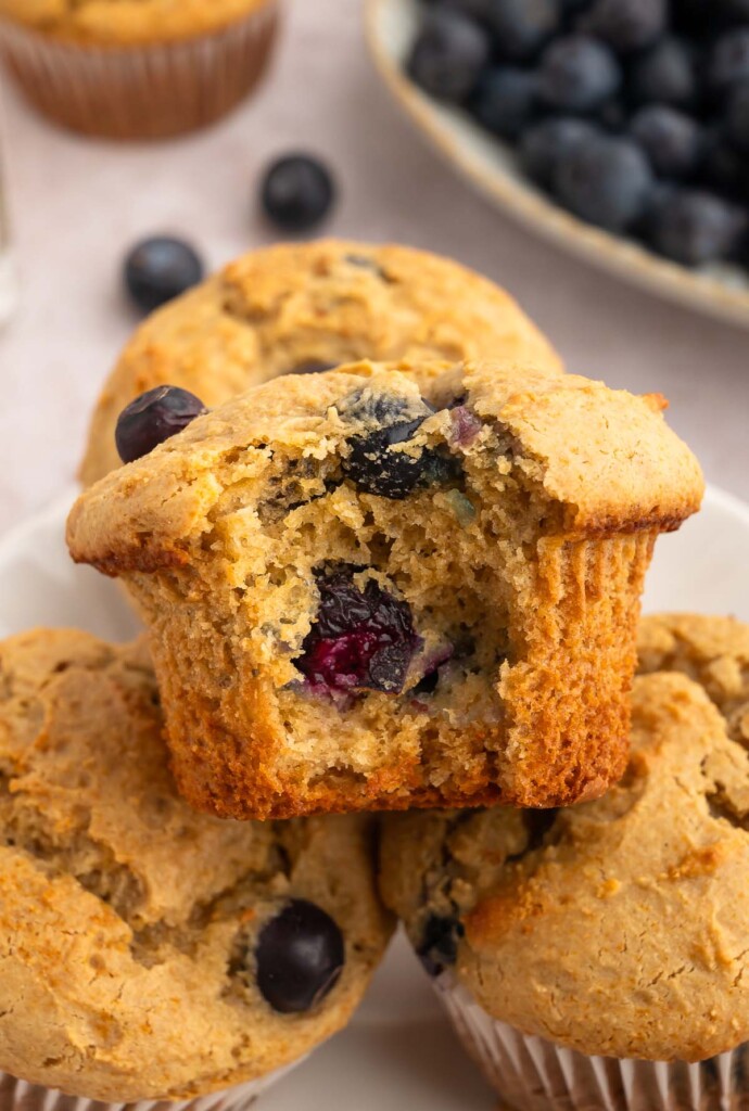 A blueberry protein muffin with a bite taken out of it with more muffins in the background.