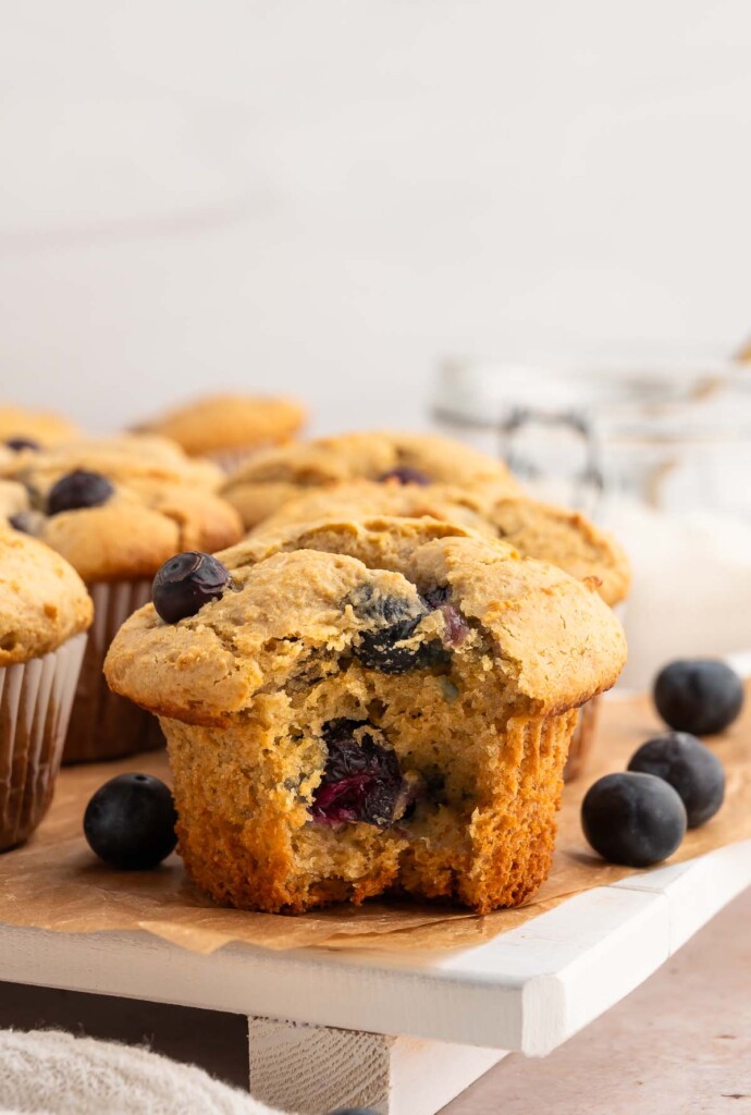 A blueberry protein muffin with a bite taken out of it with blueberries in the background.