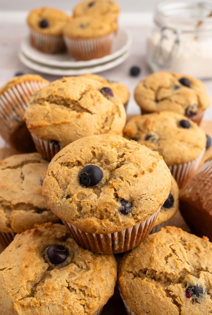 A pile of blueberry protein muffins with some in the background on a plate.