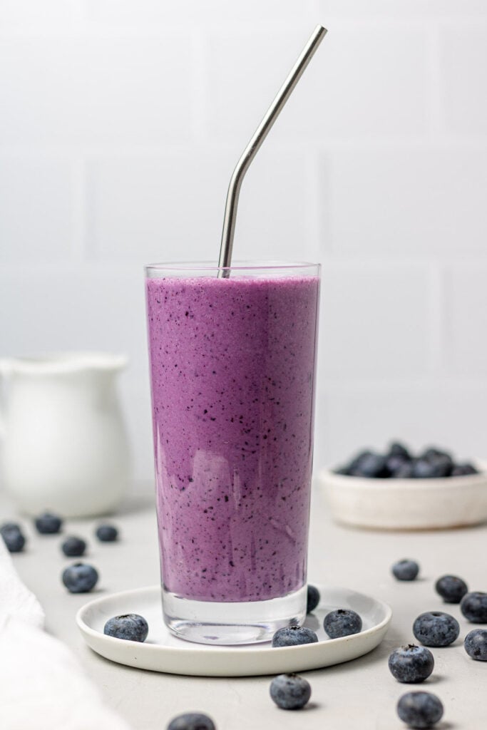 A blueberry smoothie in a clear glass with a white background