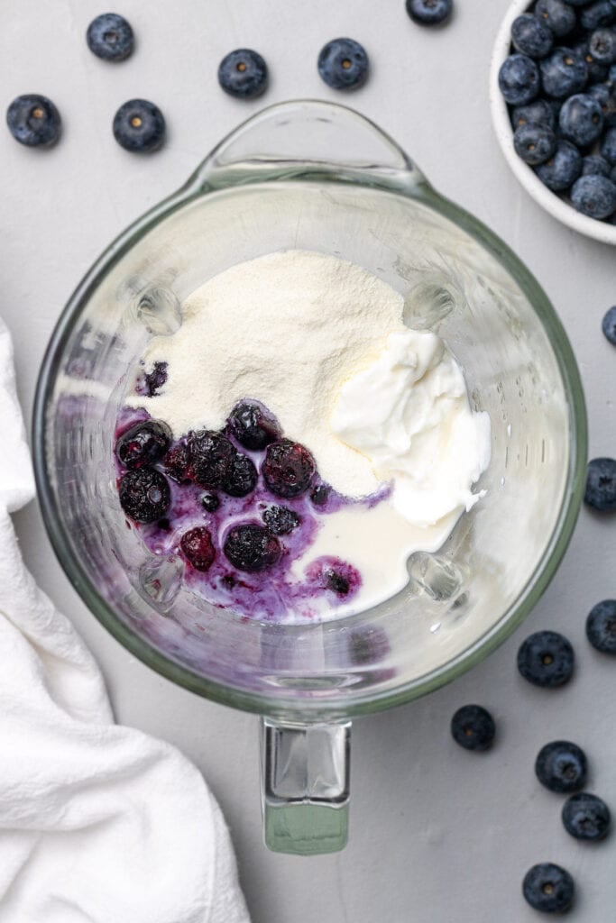 An overhead image of a blueberry smoothie in a blender on a grey background