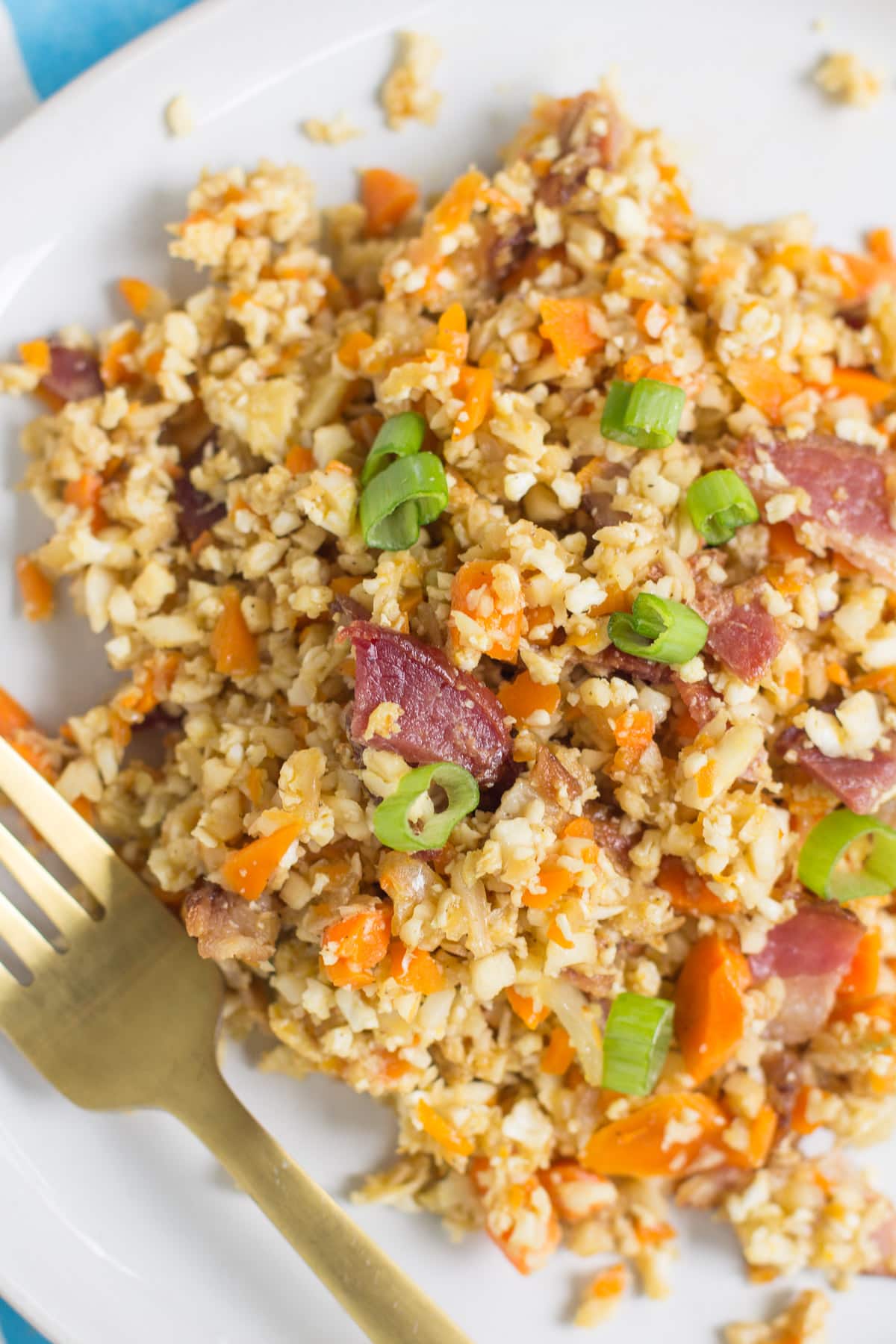 A close up of Breakfast Cauliflower Fried Rice on a white plate with a gold fork.