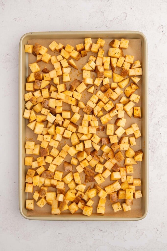 Uncooked chopped breakfast potatoes spread out on a parchment lined baking sheet. 